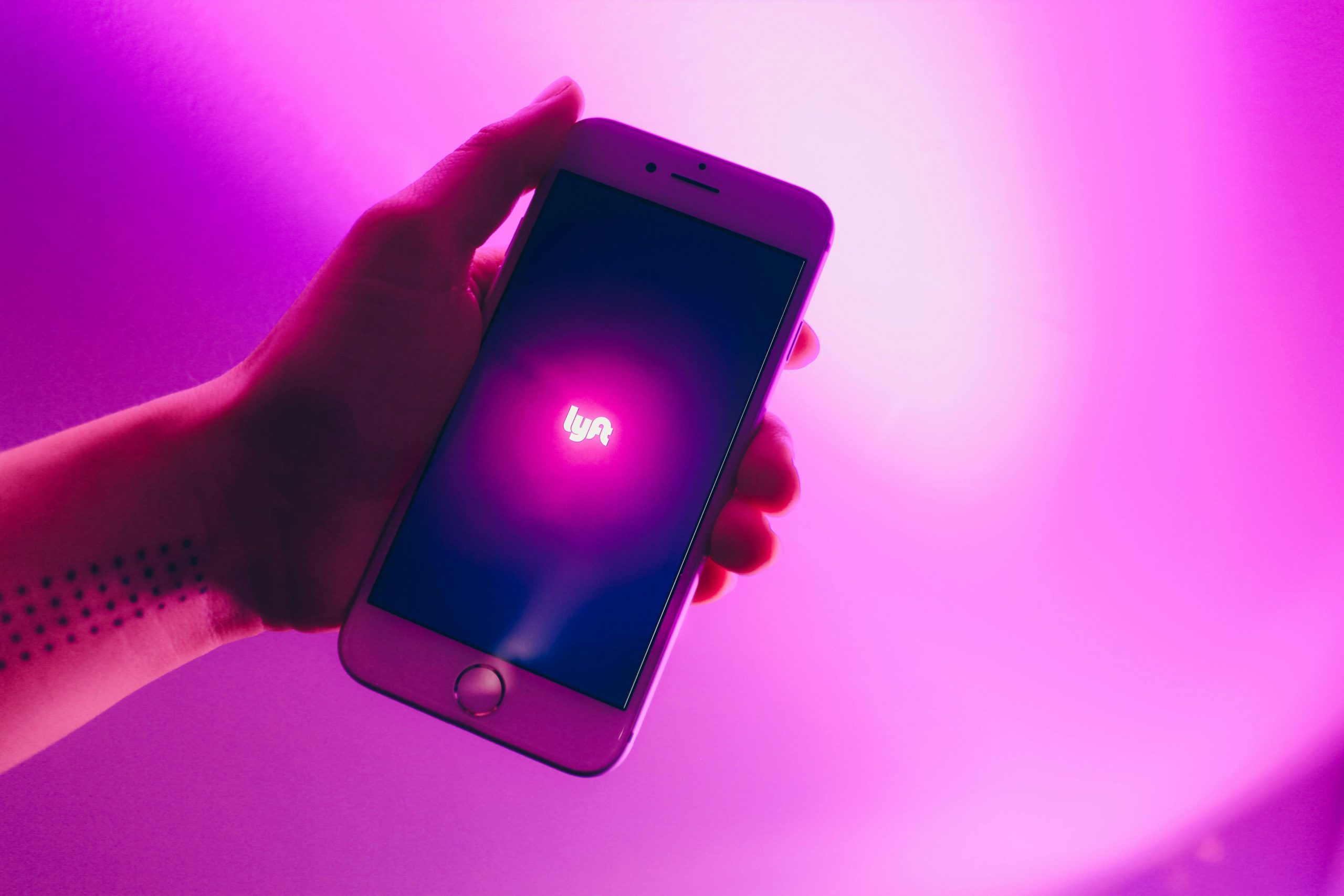 Home A hand holding a smartphone displaying the Lyft ridesharing app with a vivid pink background.